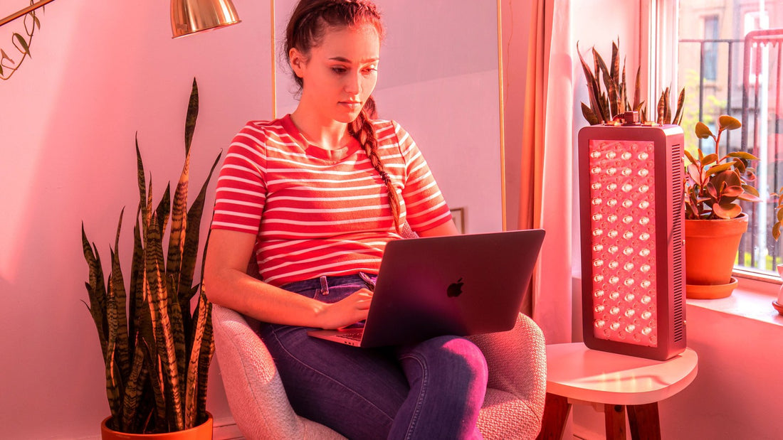 Woman working on a laptop beside a Hooga red light therapy panel