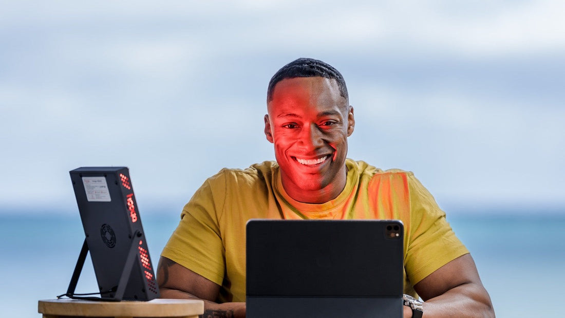 Man working at a desk beside a Hooga HG200 red light therapy panel