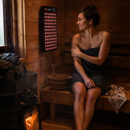 Woman in a wood-fired sauna next to a Hooga Ember red light therapy panel