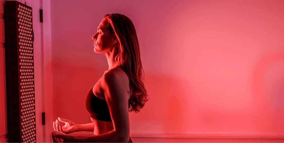 A woman sitting beside a Hooga red light therapy panel